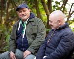 two men sat smiling together while sat on a bench