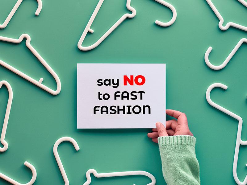 postcard saying 'say no to fast fashion'. background is light green with white coat hangers spread out around the postcard