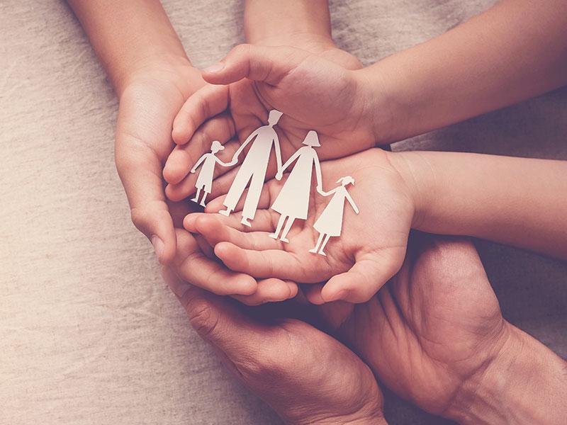 three pairs of hands piled on top of eachother with a paper family cut out on the top