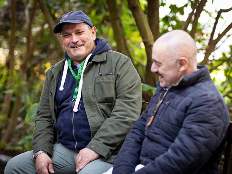two men sat smiling together while sat on a bench