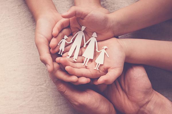 three pairs of hands piled on top of eachother with a paper family cut out on the top